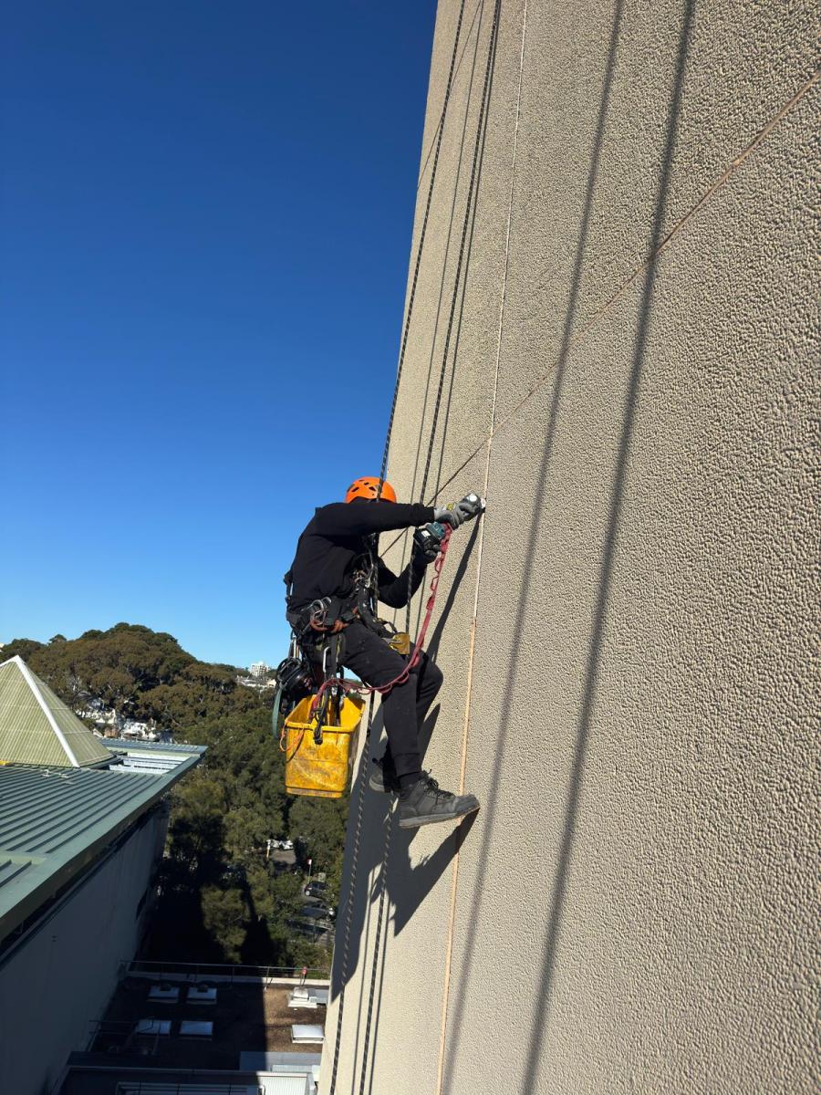 Professional rope access technician abseiling down high-rise building wall with safety equipment and tools