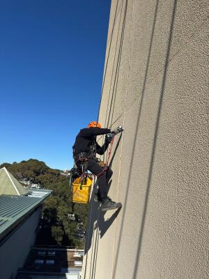 Professional rope access technician abseiling down high-rise building wall with safety equipment and tools