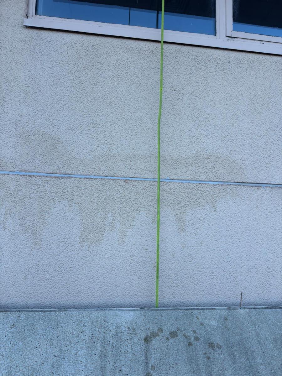 Green rope access equipment line against grey concrete building facade with windows and panel joints