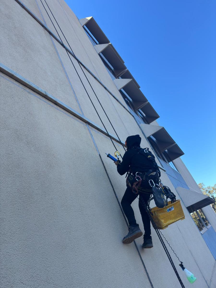 Rope access technician abseiling down modern commercial building facade with safety equipment and tools