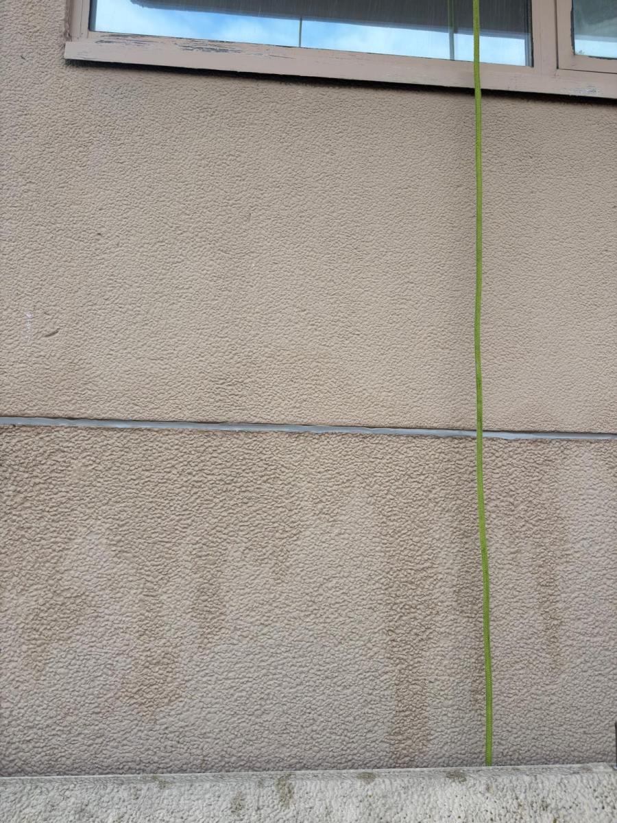 Green rope access safety line against beige rendered building facade with window above