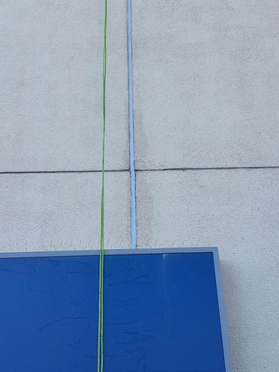 Close-up of grey concrete building facade showing worn sealant joints and blue architectural element requiring maintenance