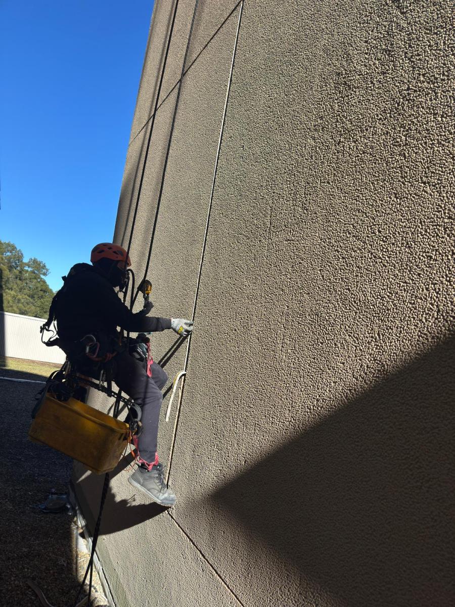 Rope access technician working beside a textured high-rise building façade with a tool bucket
