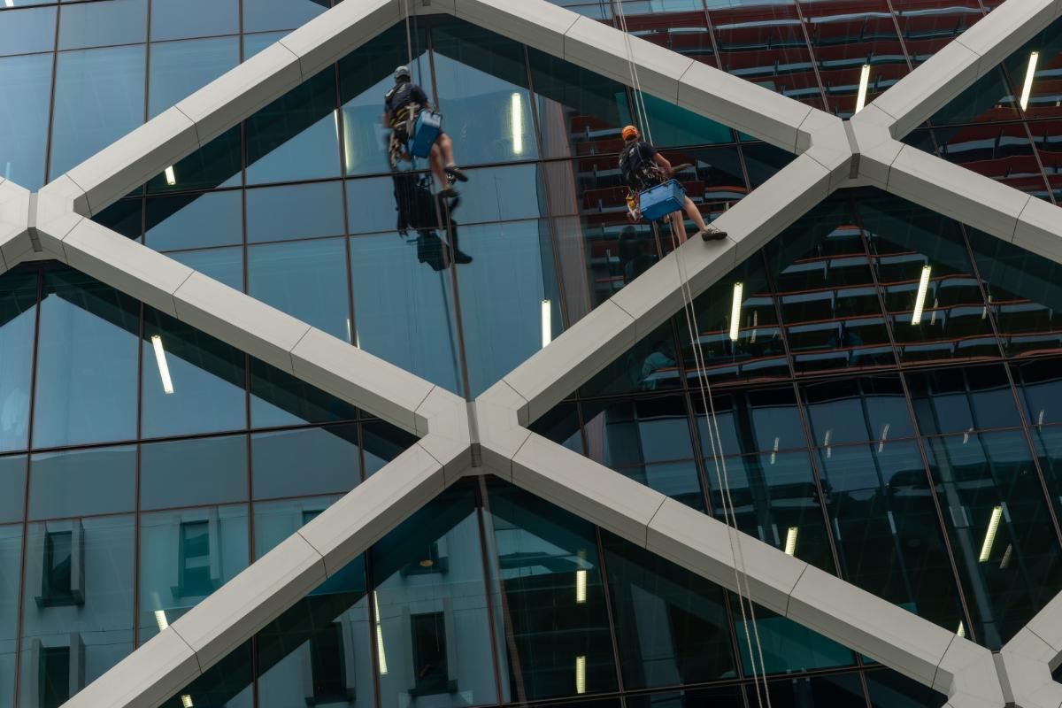 Two rope access technicians abseiling down modern glass office building performing window cleaning maintenance