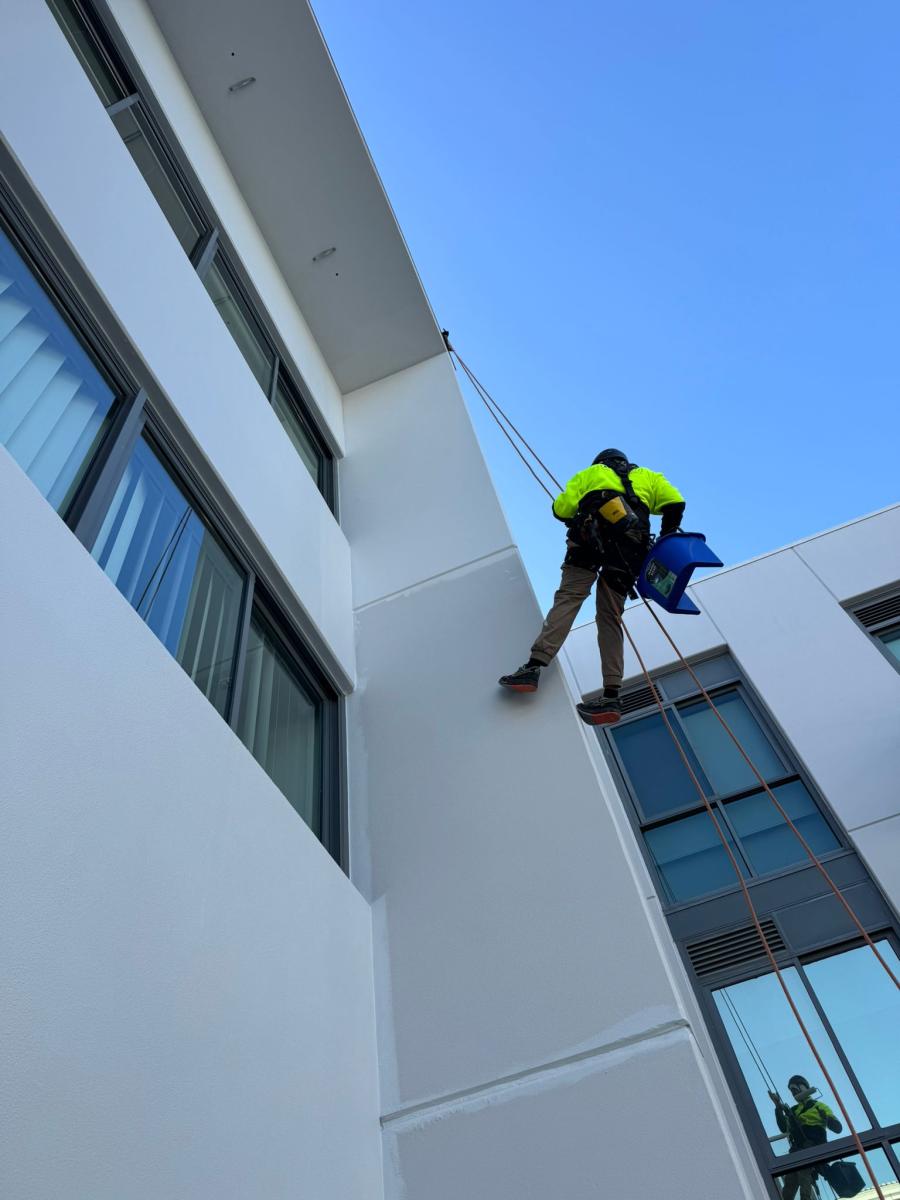 Professional rope access technician in high-vis clothing cleaning windows on modern white commercial building facade
