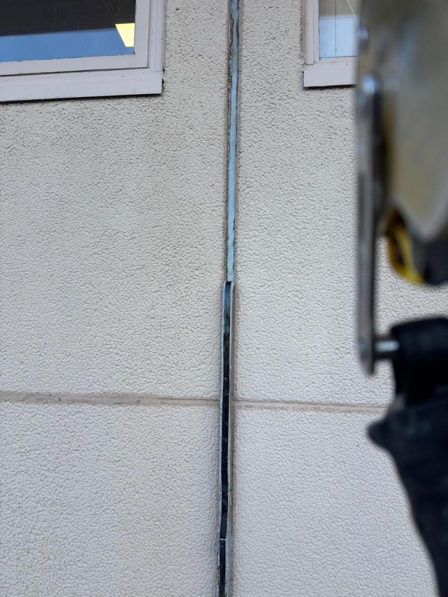 Close-up of cracked exterior wall sealant showing gap requiring rope access maintenance and repair work