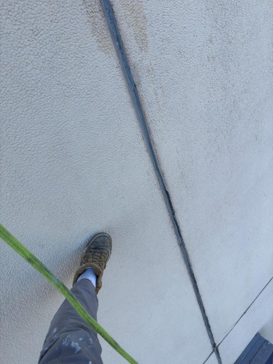 Rope access technician&#039;s view from height showing safety boot and green rope on concrete building surface
