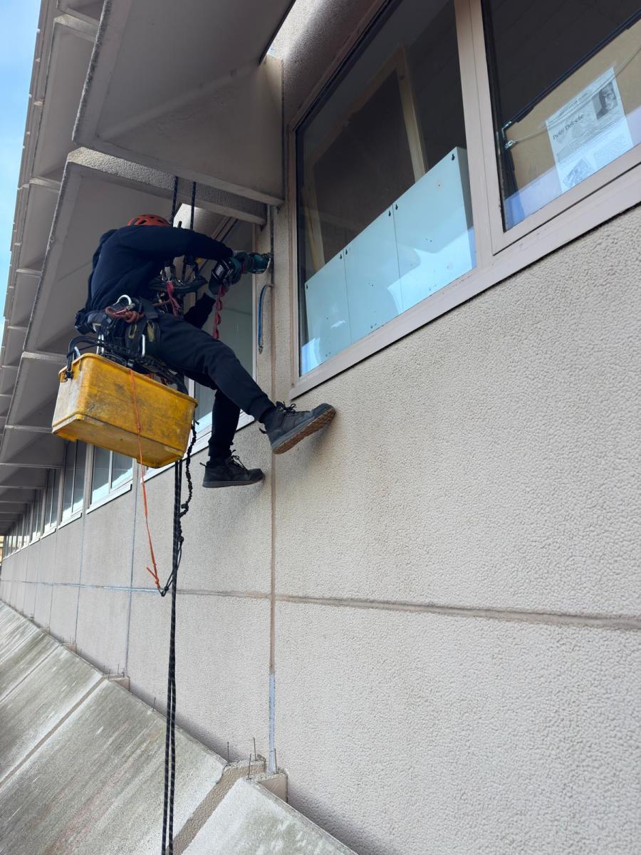 Professional rope access technician in safety harness performing building maintenance work on high-rise facade