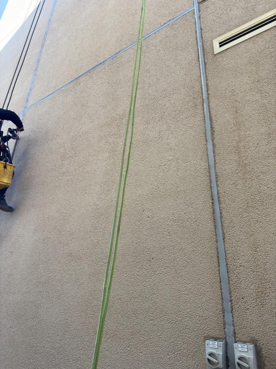 Rope access technician abseiling down beige building facade during professional rendering maintenance work